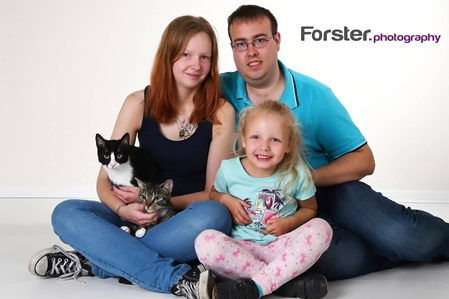 Junges Paar mit Kind und Katze lächelt beim Fotoshooting in die Kamera