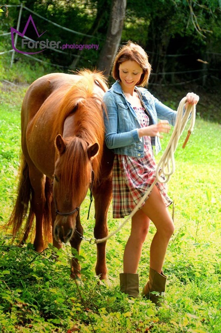Junge Frau im Sommerkleid mit braunem Pferd auf einer grünen Wiese